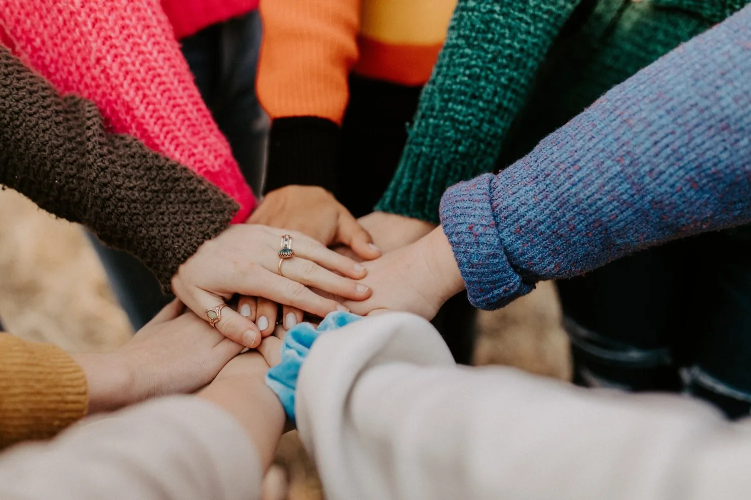 A group of people in colourful jumpers stacking their hands together in a circle
