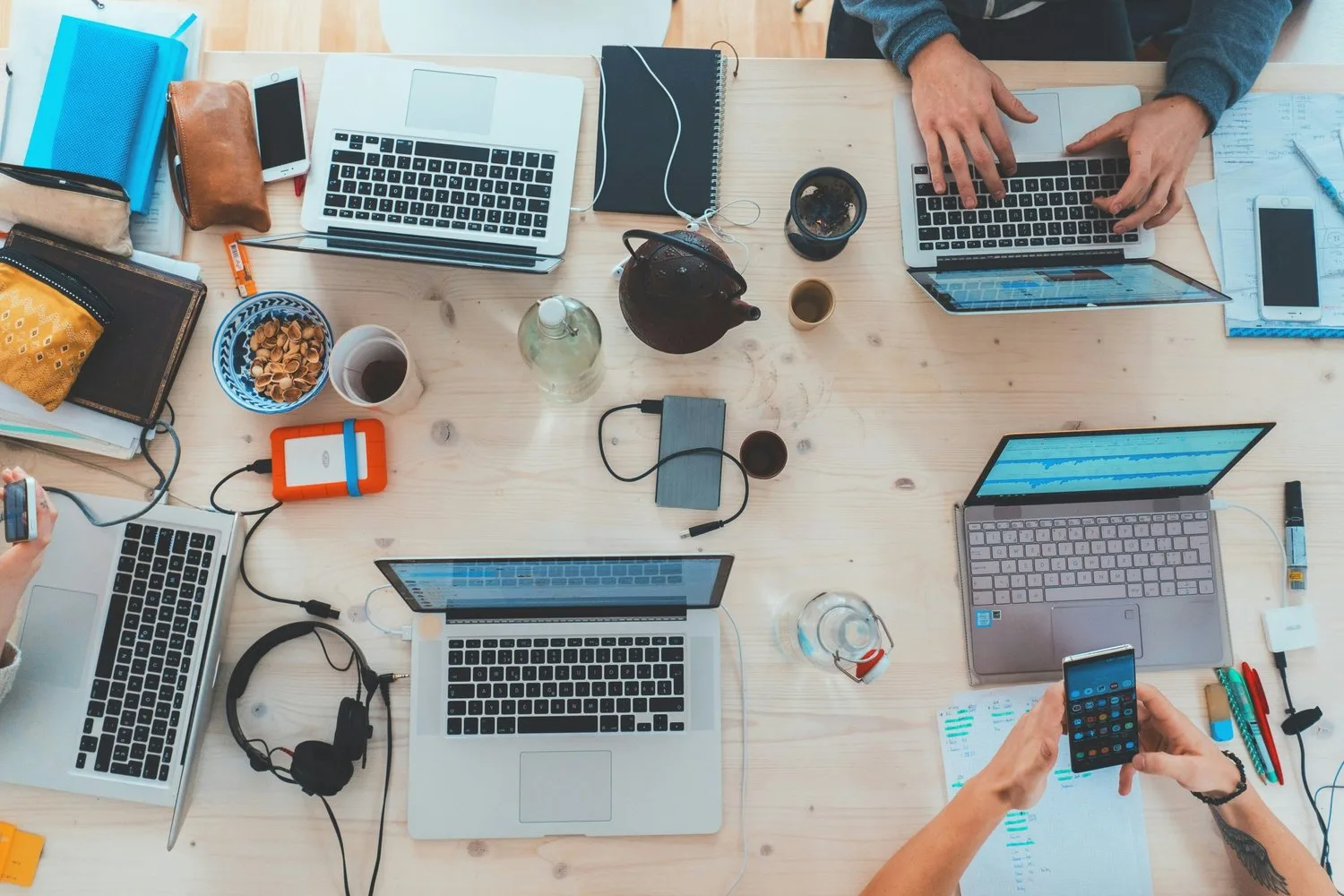 Overhead view of a shared desk with laptops, phones and notebooks as a group works together